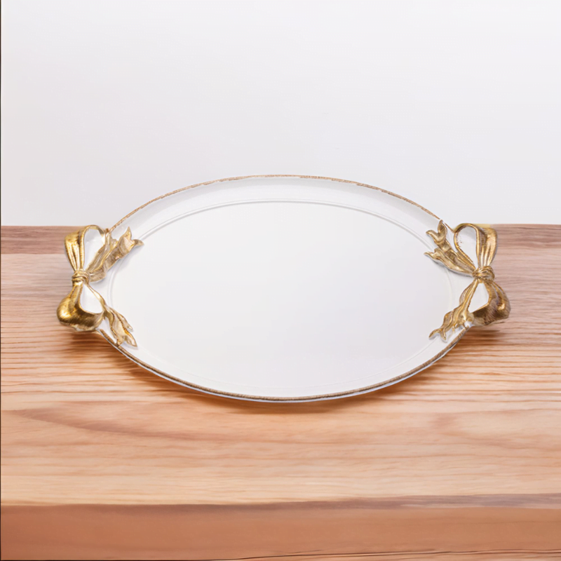 A white tray with gold accents and ribbon handles on a wooden table.