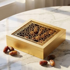Gold decorative box with intricate arabesque lattice lid filled with dates, displayed on marble surface with scattered dates alongside