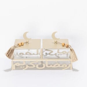 Cream metal serving stand with Ramadan Kareem calligraphy cutout, holding two clear lidded acrylic boxes with tassel details.